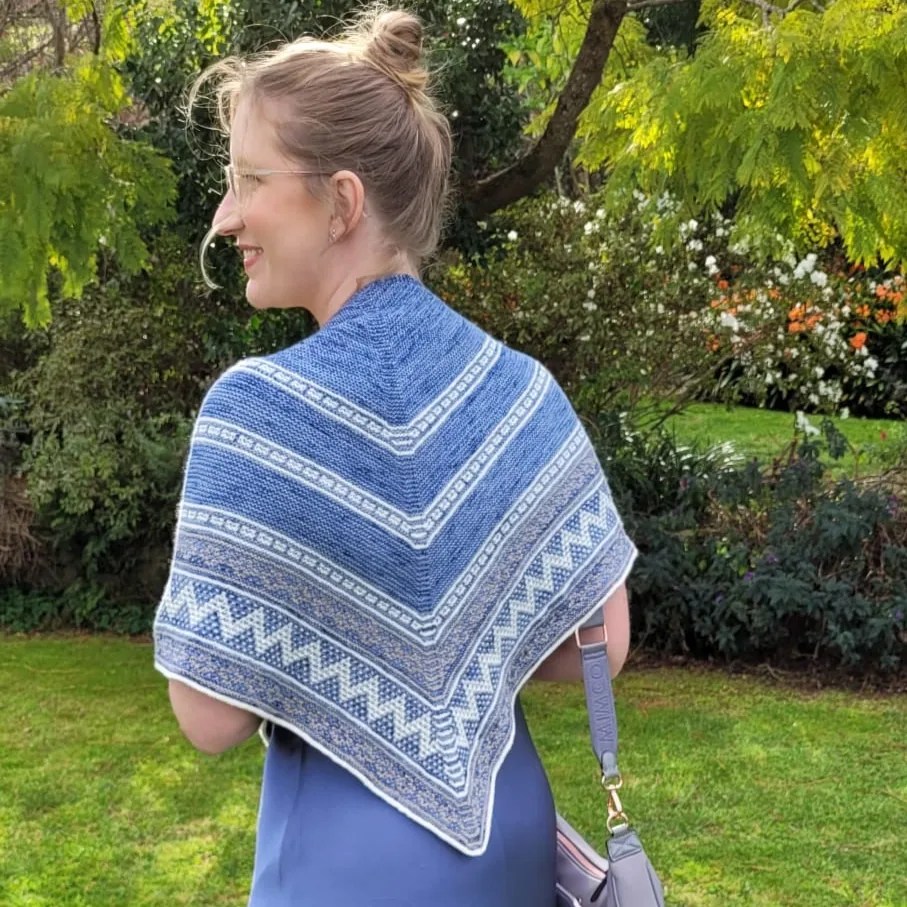 The author Hope has her back to the camera, is in a pastel blue dress with a blue and white knitted shawl draped over her shoulders. 